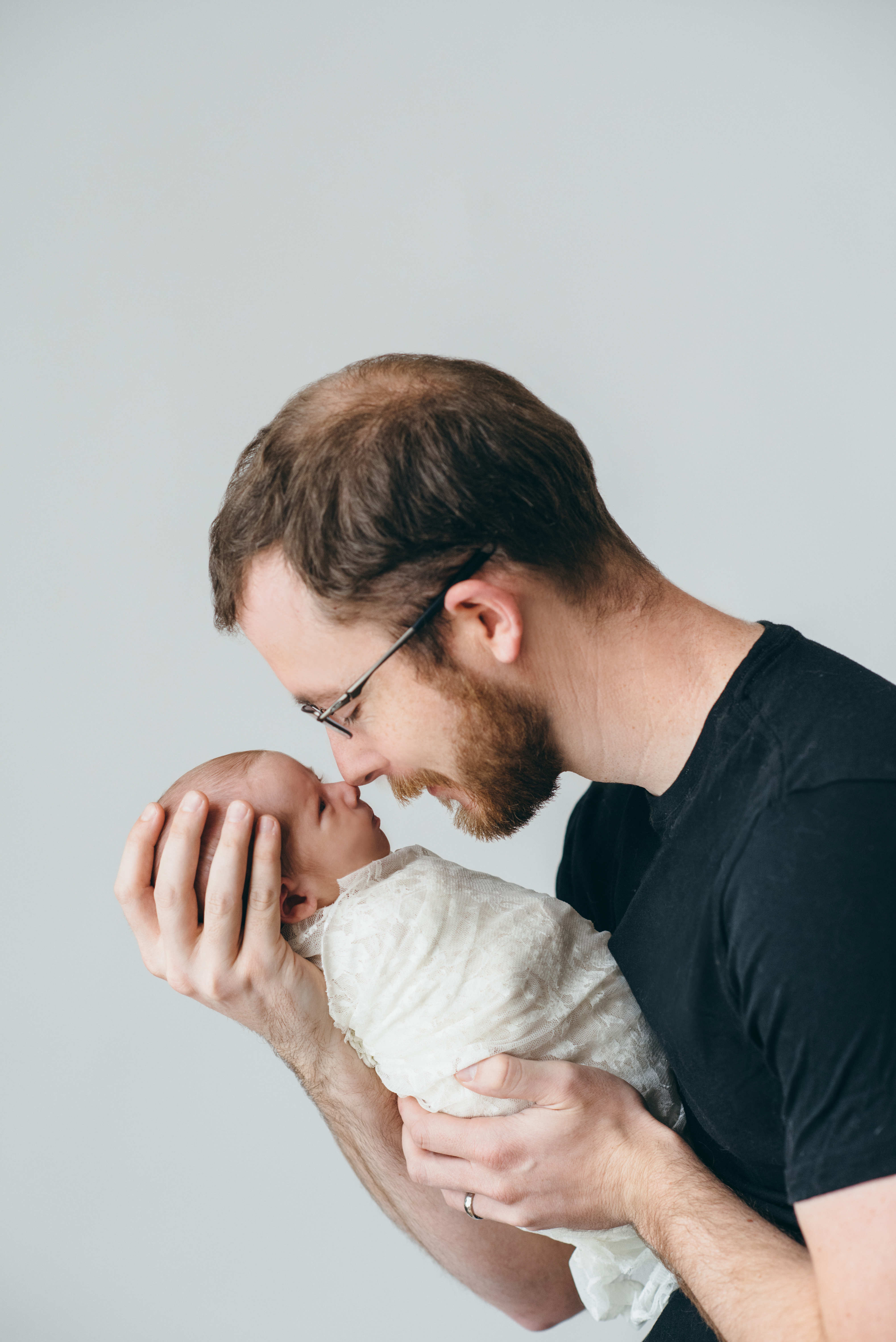 bearded father wearing glasses, touching noses with newborn daughter